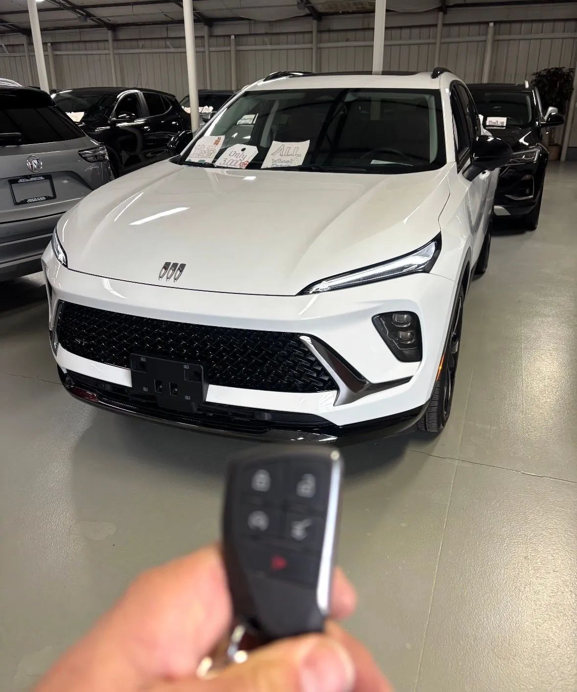 Hand holding a car key fob in front of a white SUV inside a showroom