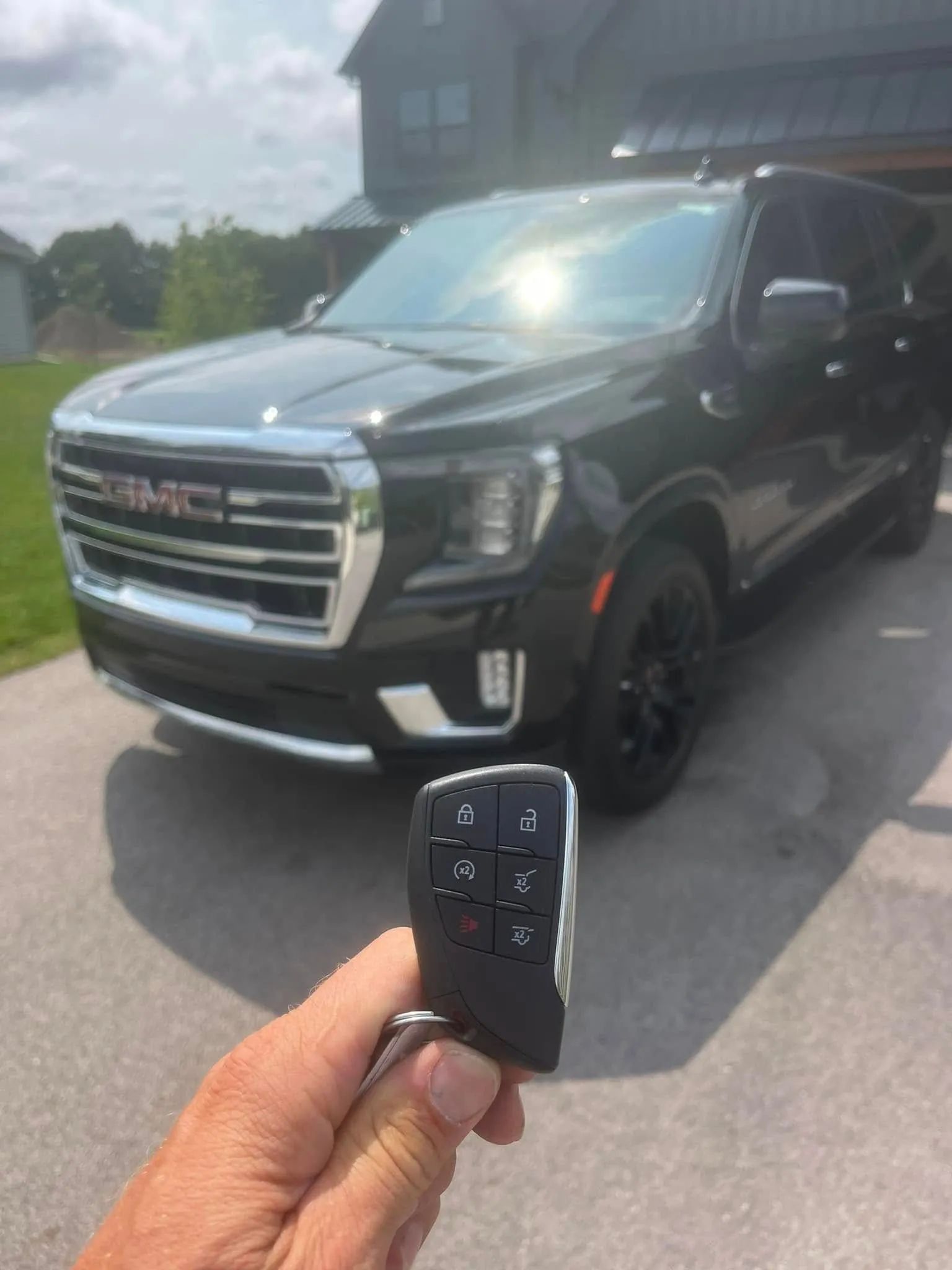 Black GMC SUV parked on a street, with a hand holding the key fob in the foreground.