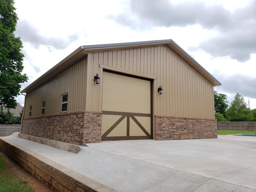 Tan metal garage with a brick base, brown door, and concrete driveway.