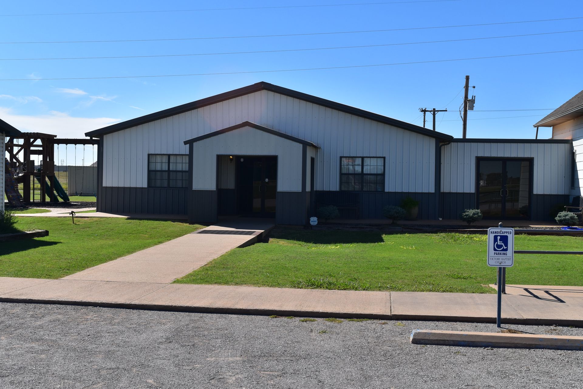 A one-story building with a pathway, grass, and a handicap parking sign.