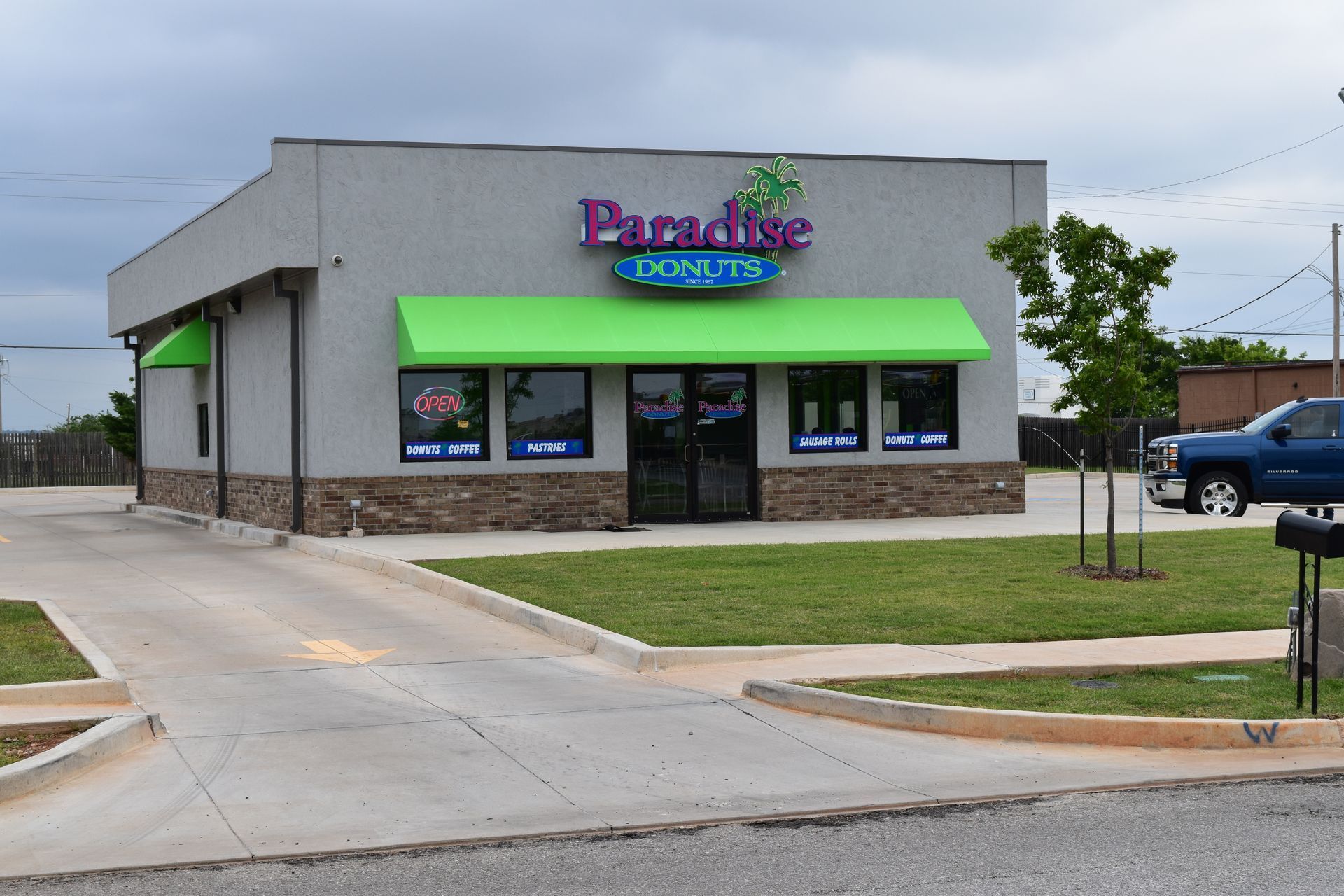 Paradise Donuts shop with green awning, neon sign, and drive-thru in a commercial building.