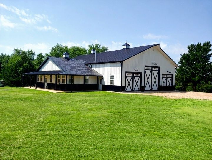 White and black barn with a porch on green lawn under a blue sky.
