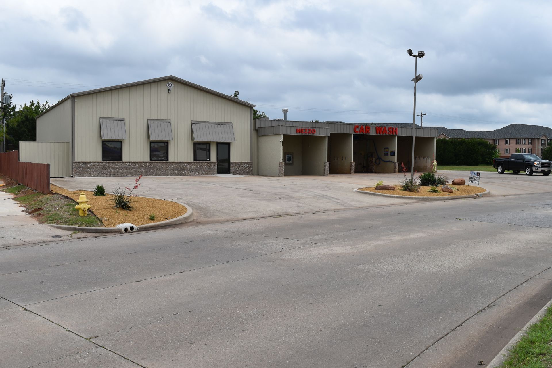 Car wash building under a cloudy sky, with drive-through bays, and open parking in front.