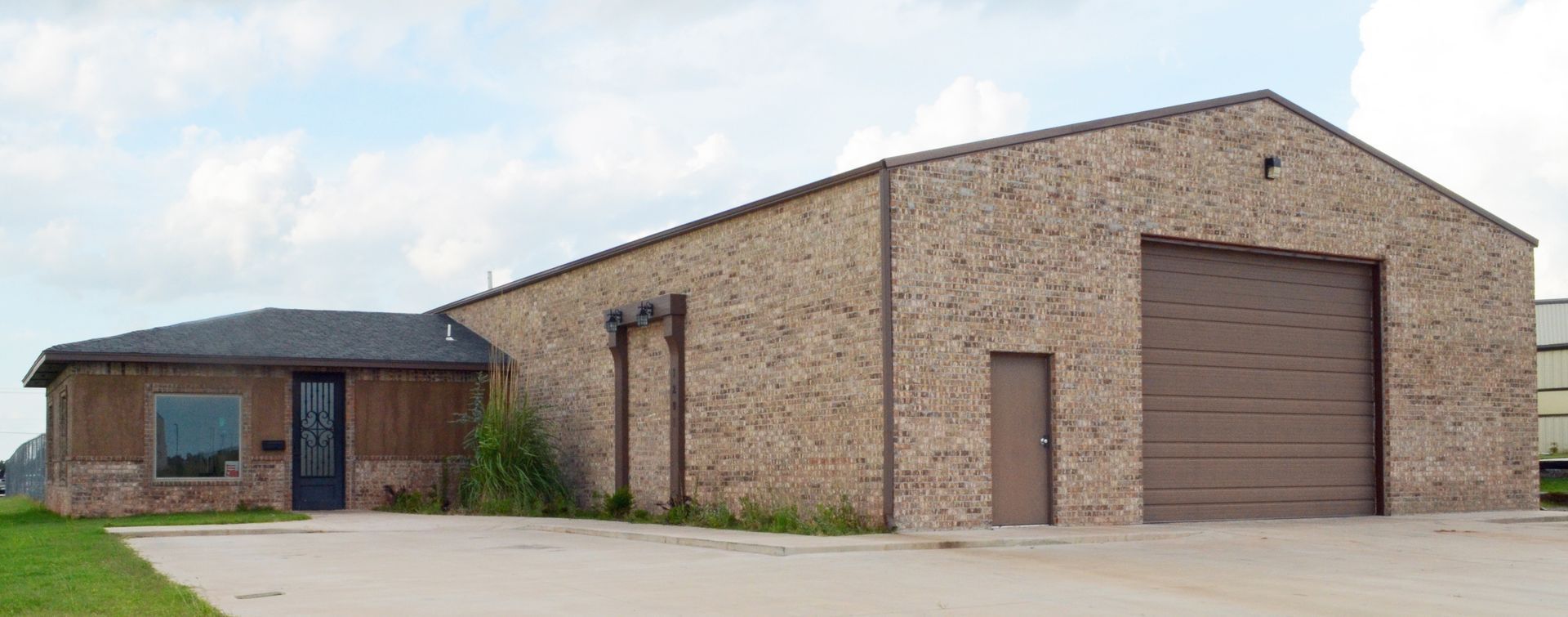 A building with a small office attached to a larger warehouse, all tan brick with a dark garage door, blue sky.