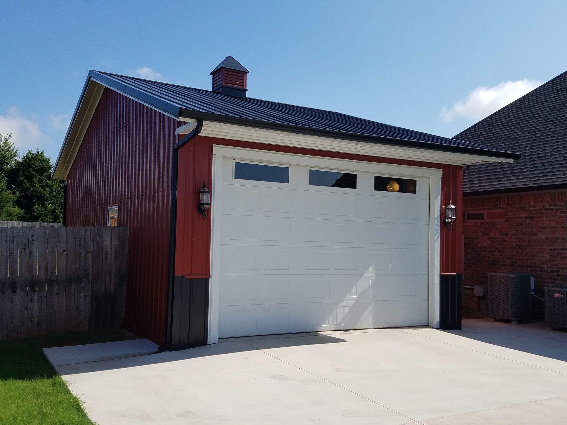 Red metal garage with white door, black roof, and concrete driveway.