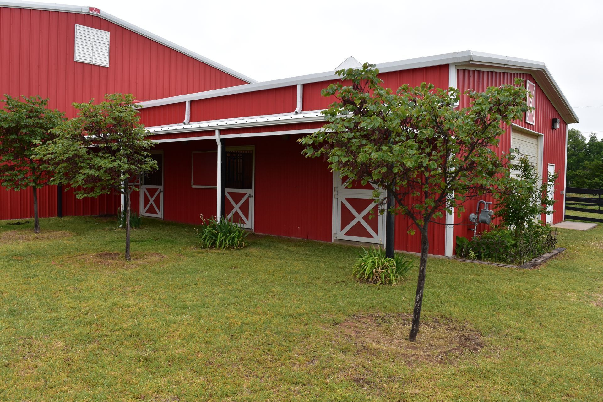 Red barn with white trim, trees in front, green grass.