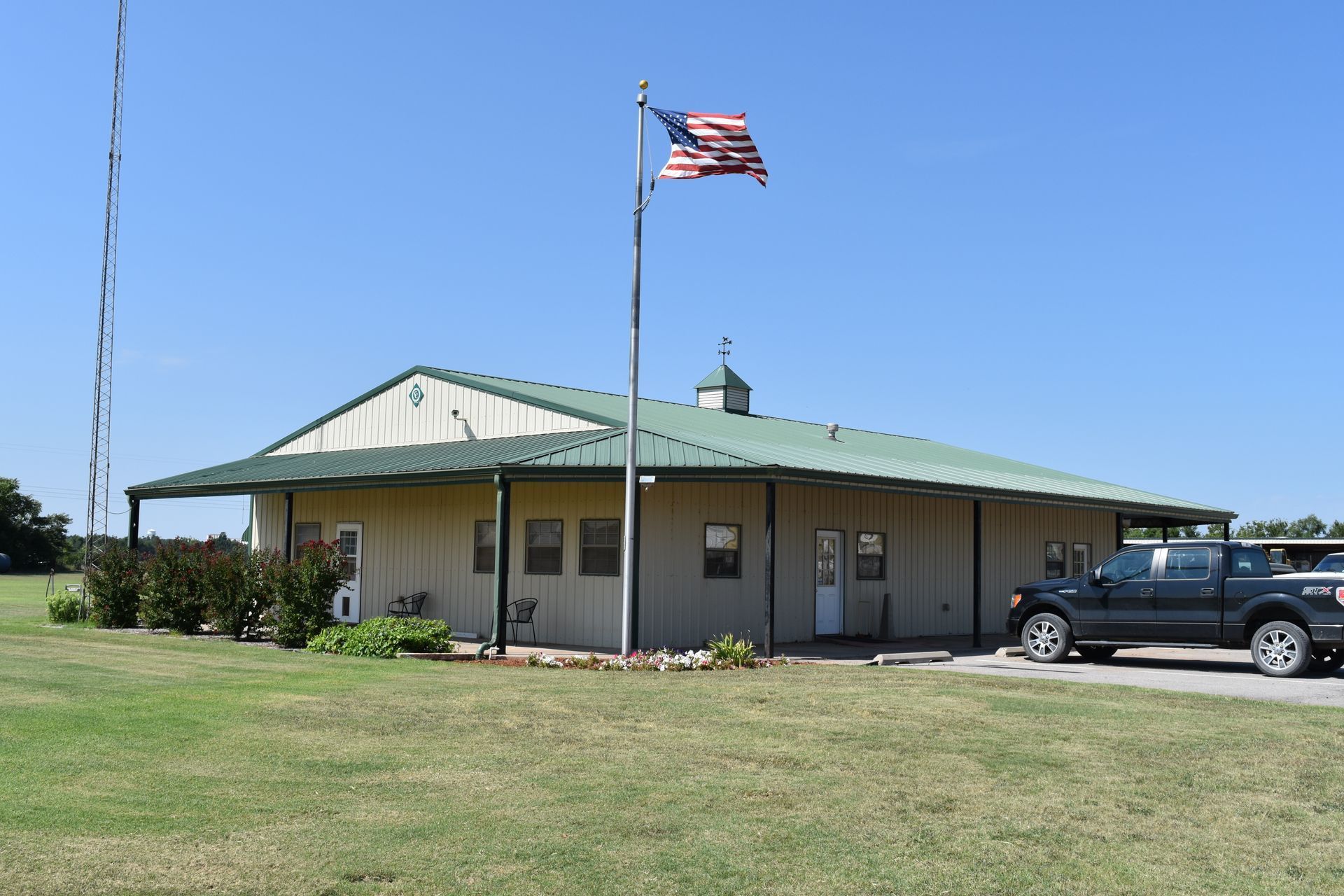 A one-story building with green roof, American flag, and truck parked outside on a sunny day.
