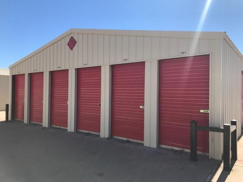 Storage units with red doors, tan siding, and a blue sky.