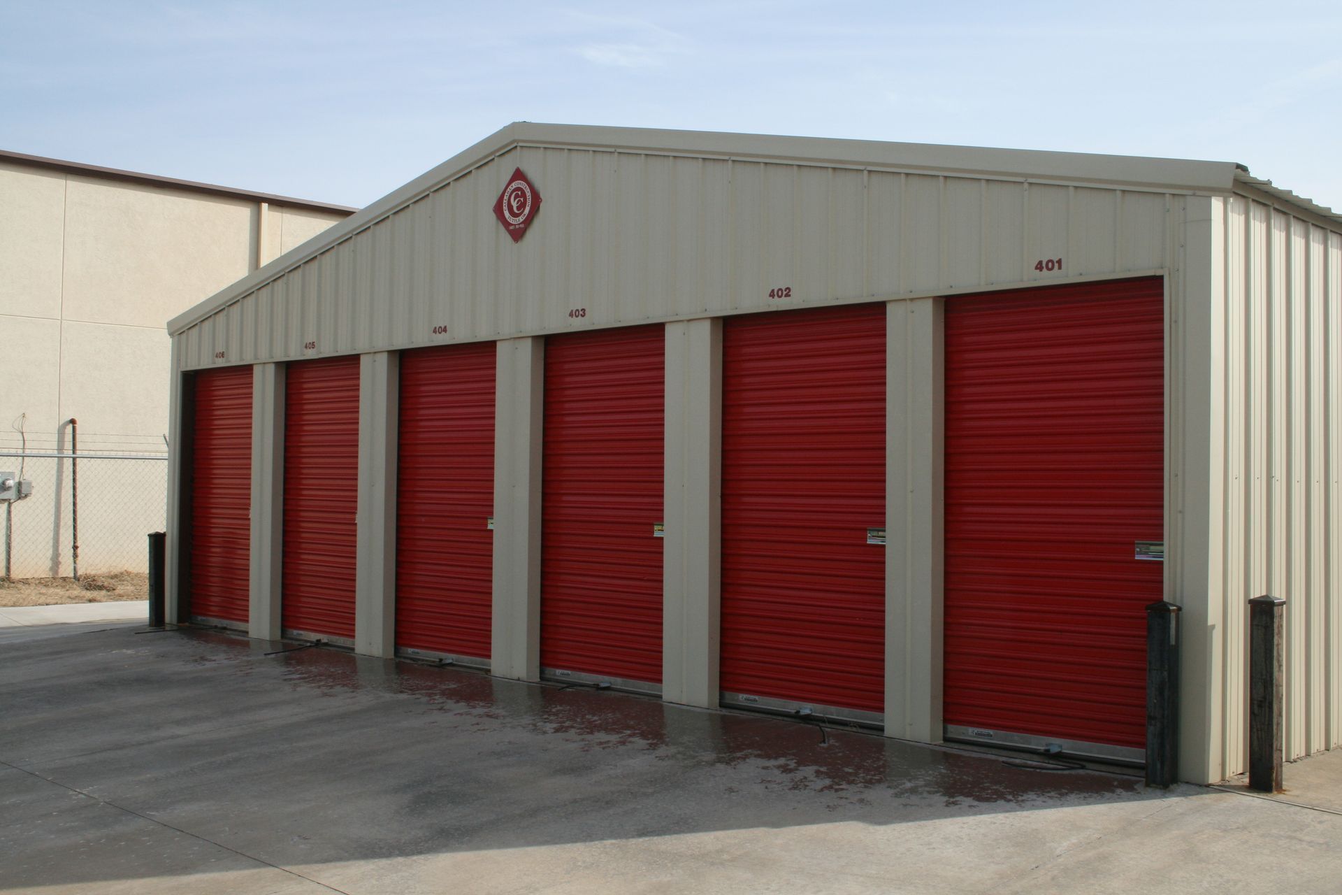 Storage units with red doors, beige metal siding, under a blue sky.
