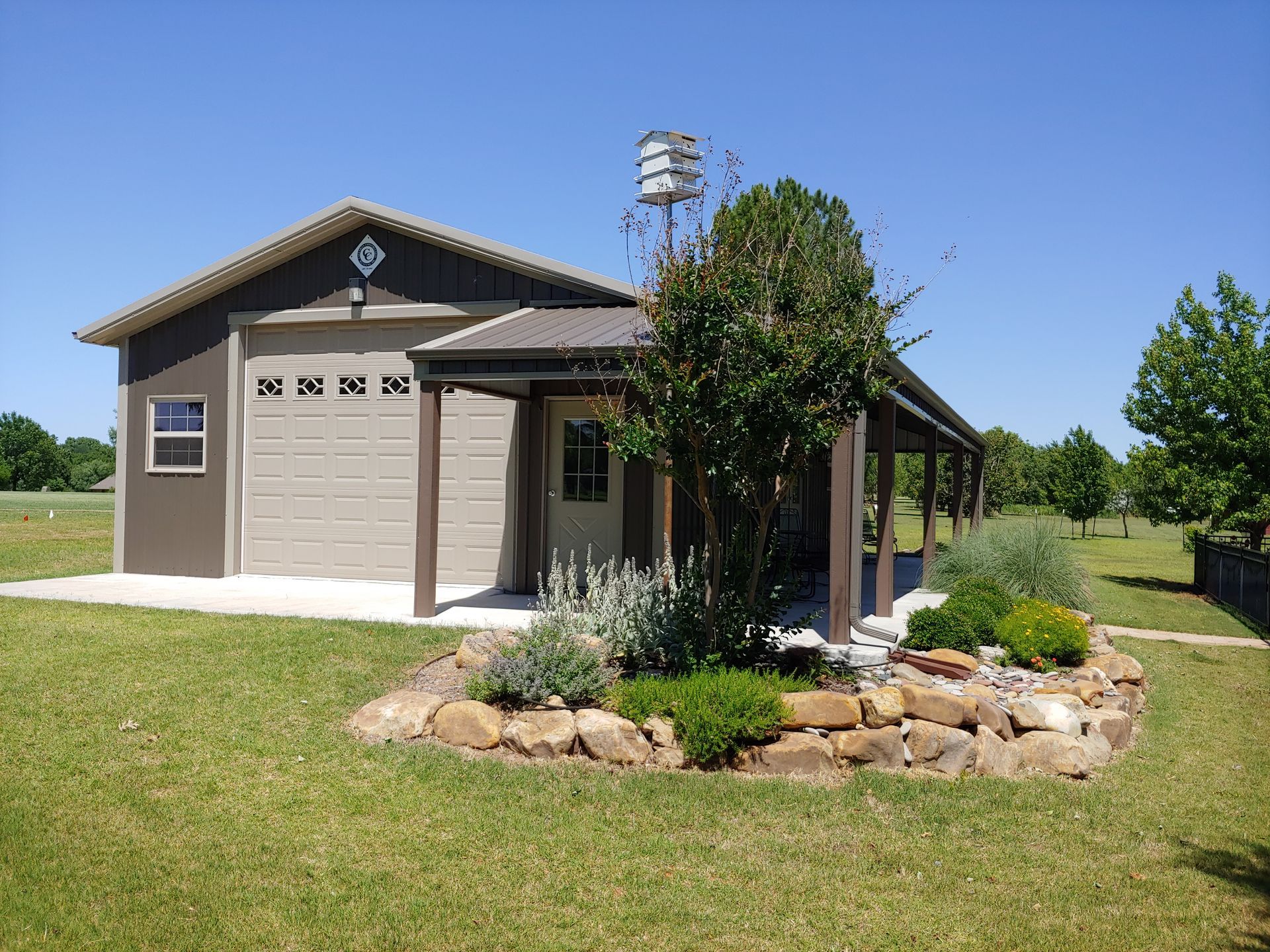 Garage with brown accents, porch, and landscaping on a sunny day.