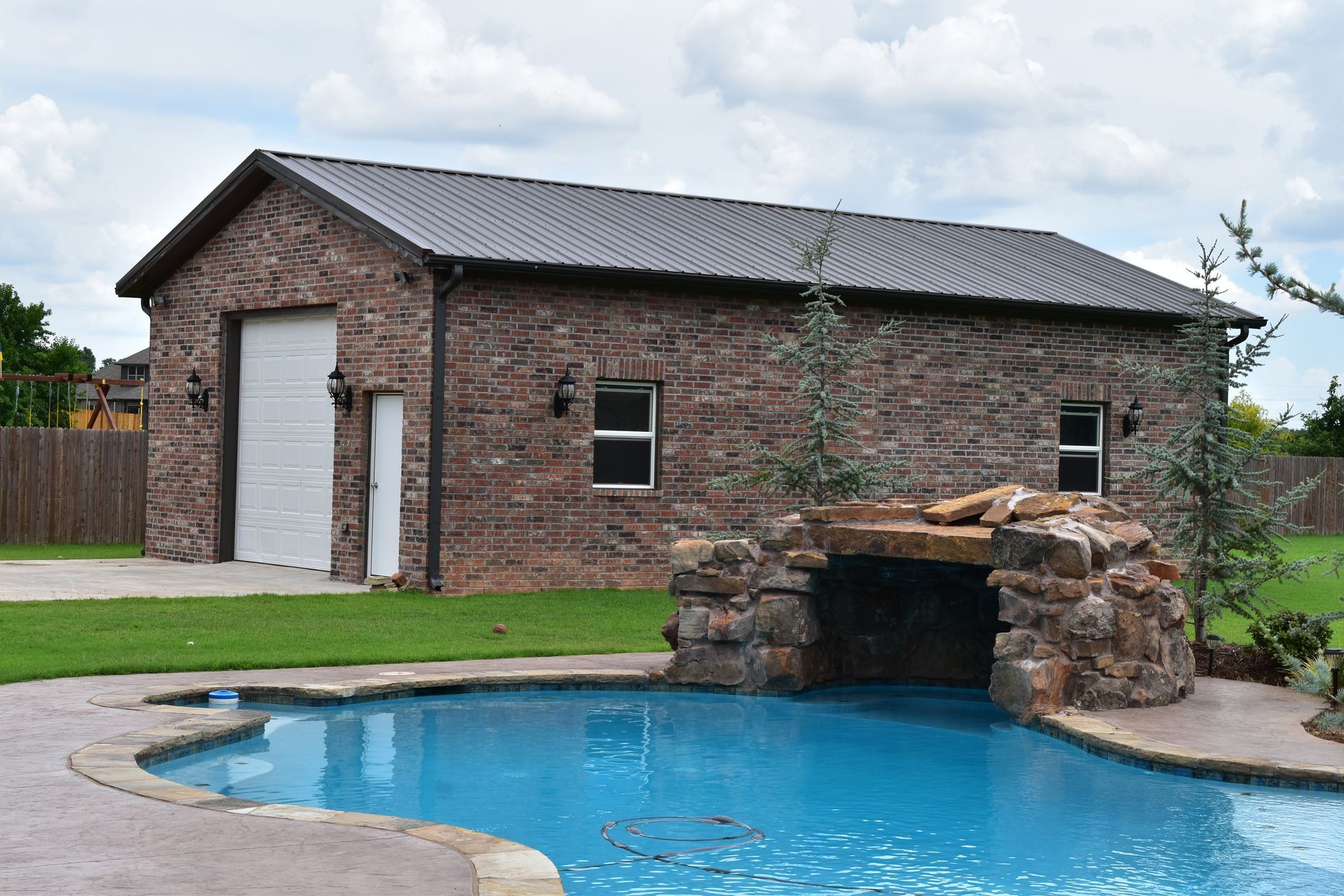 Brick building with a garage door, small windows, and a pool with a rock waterfall.