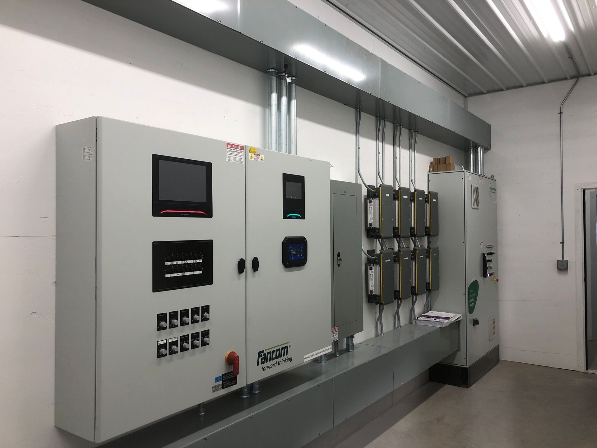 Control panel equipment on a white wall in a room. Gray metal panels with screens and wiring.