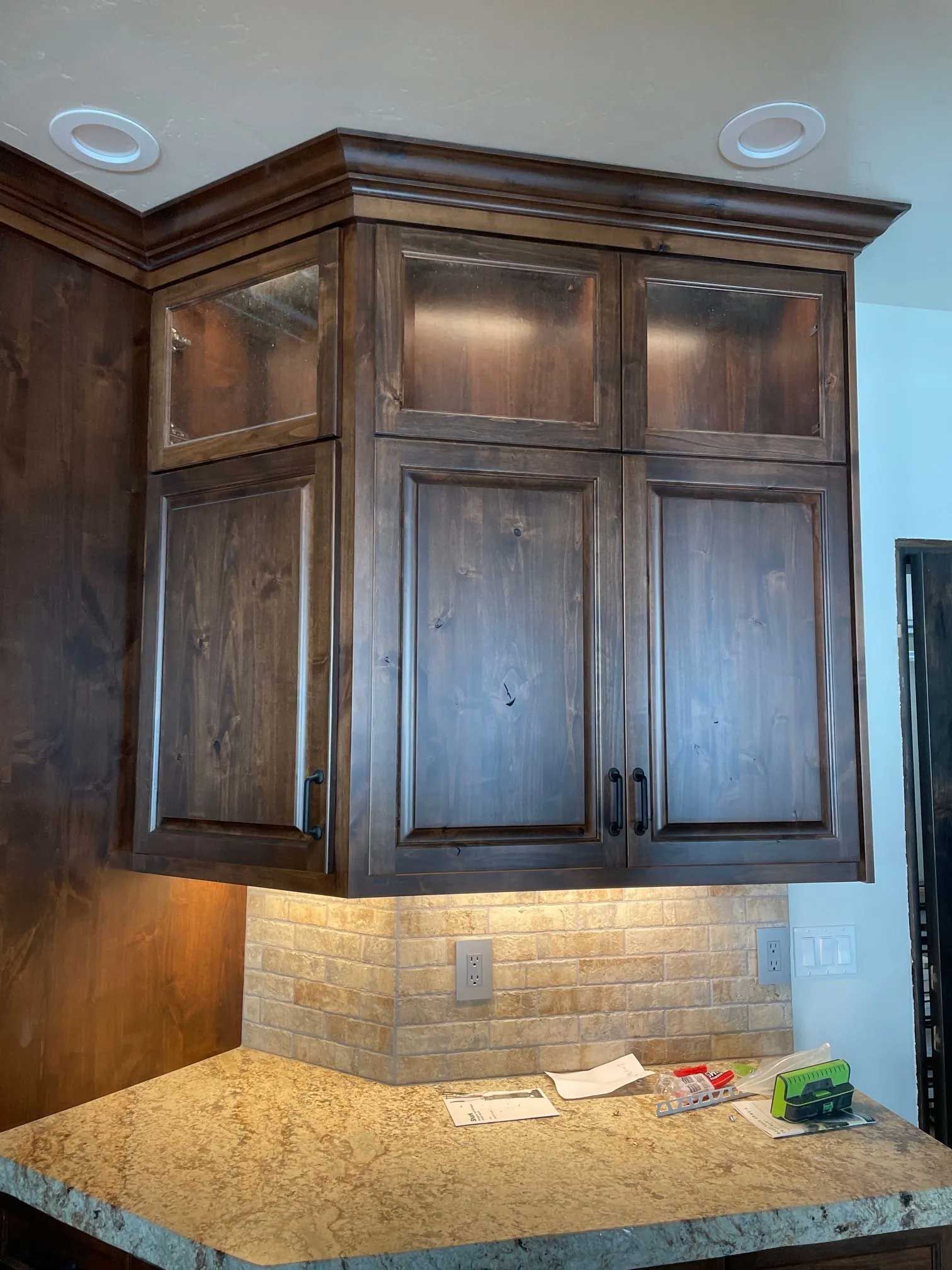 Kitchen cabinets with wood finish, glass doors, above a tiled backsplash and countertop.