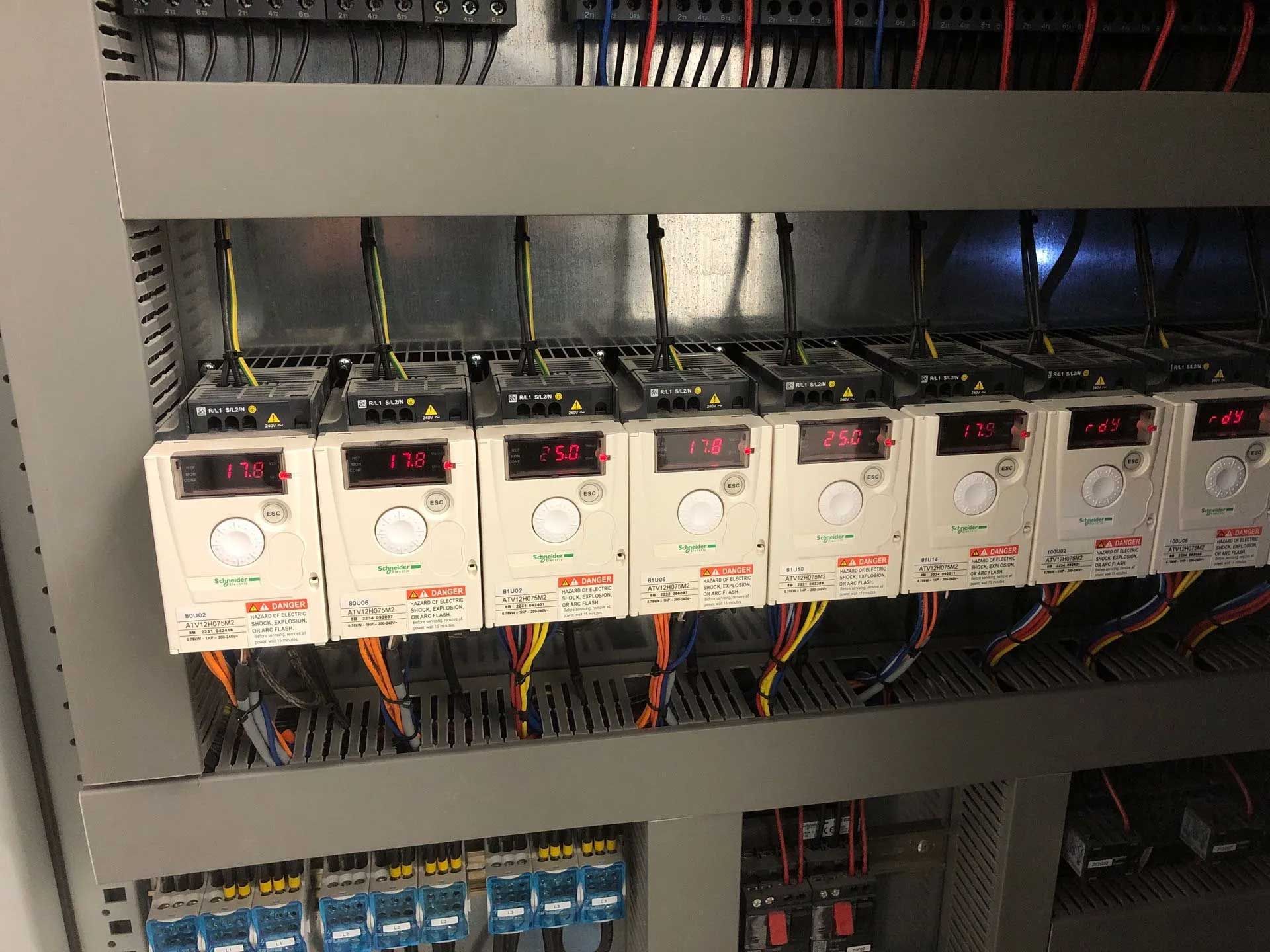 Row of industrial controllers mounted in a panel. Each has a digital display showing a number. Wiring is visible.
