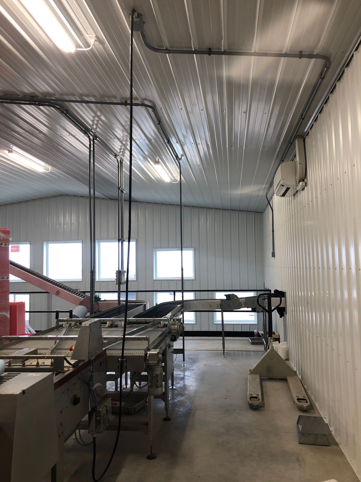 Interior of a food processing facility with machinery, white walls and ceiling, and conduit.