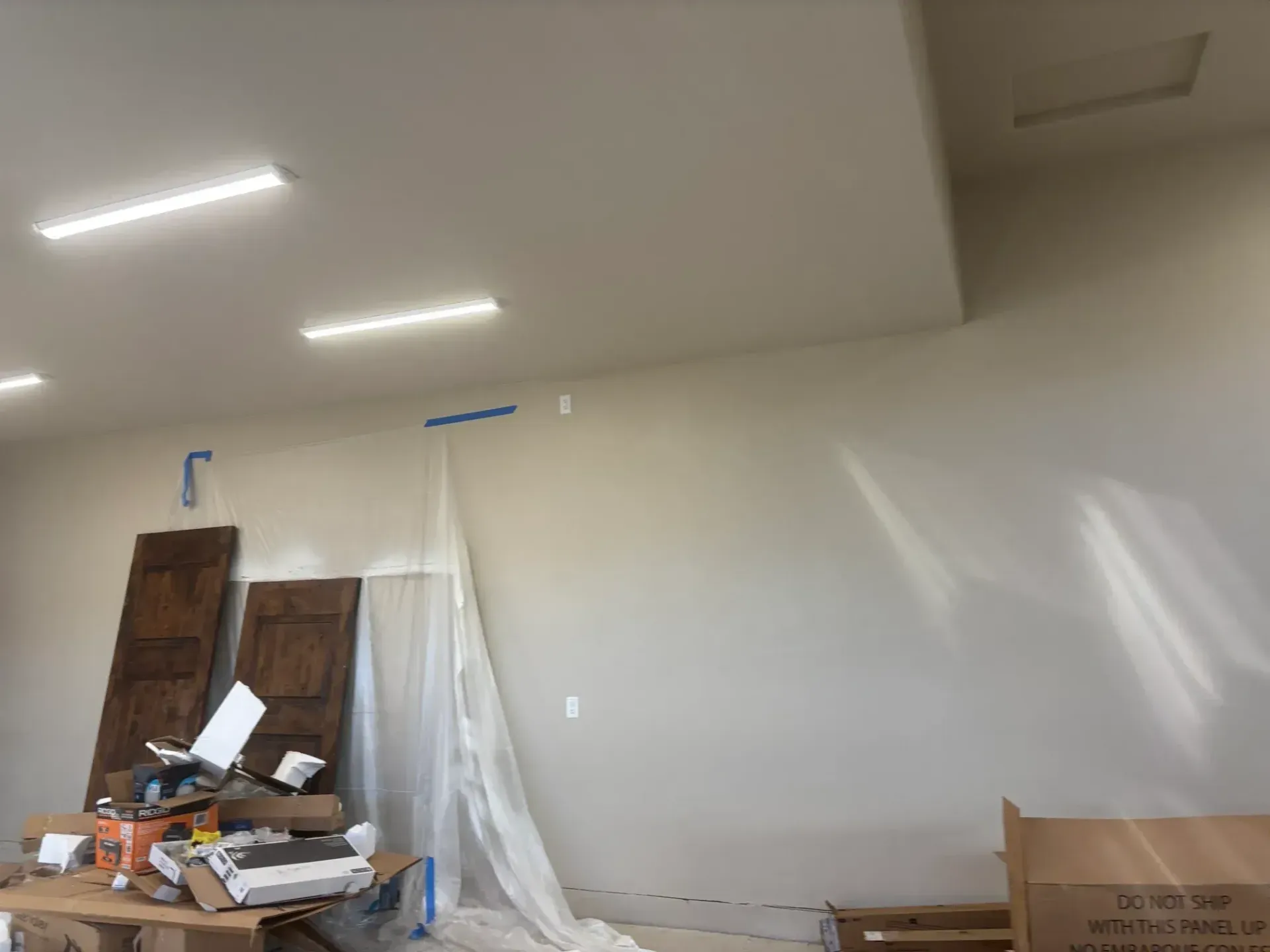 Interior of a room under construction with paint supplies, wood panels, and a drop cloth on a wall.