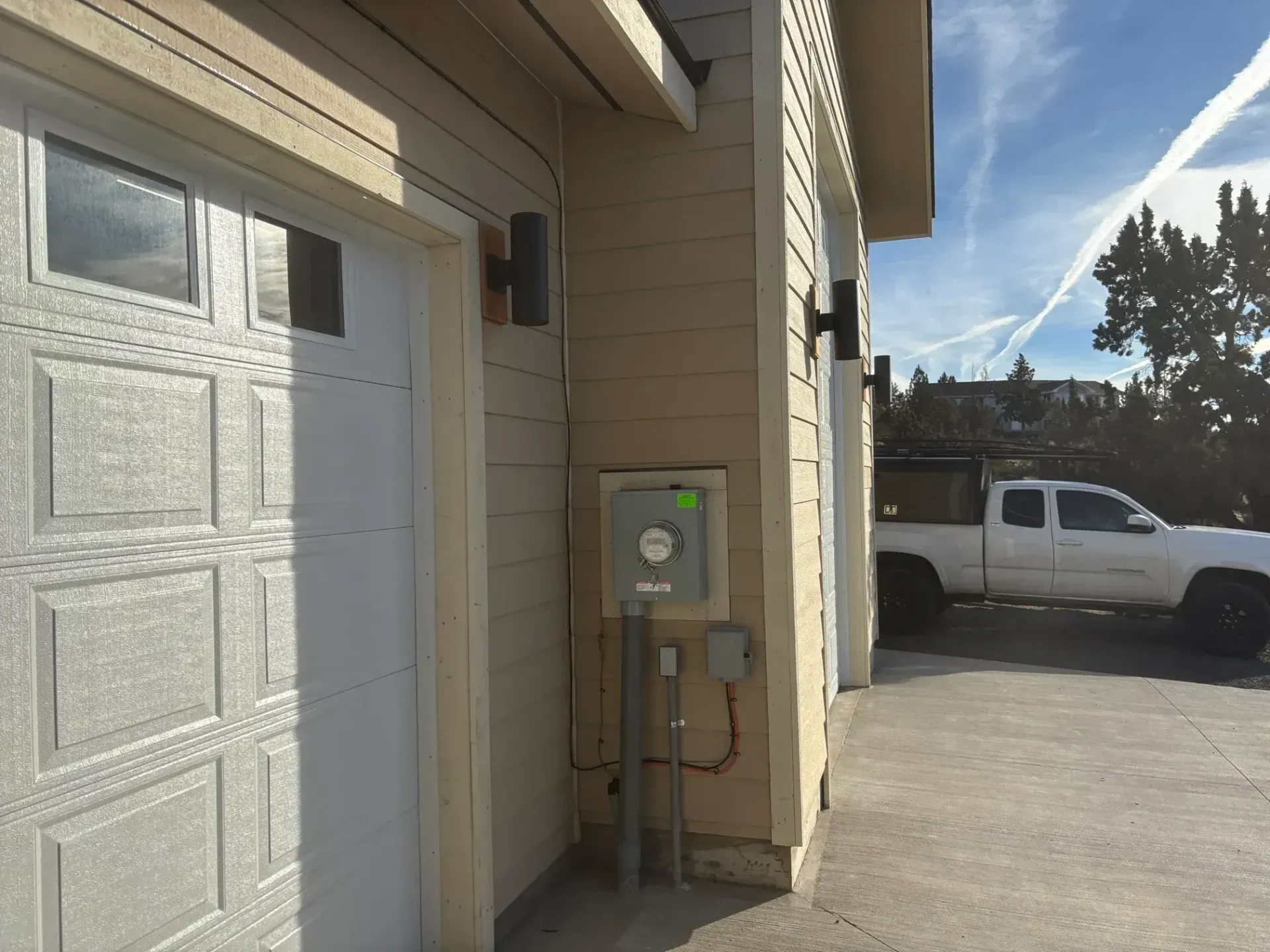 Garage exterior with a light beige door and a grey electrical panel. A white truck is parked nearby.