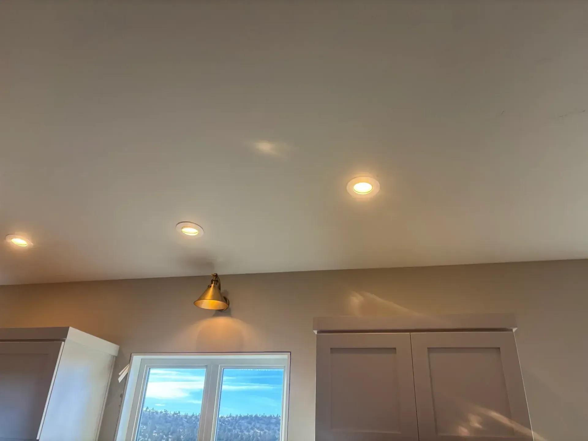 Ceiling with recessed lights, and a pendant light fixture over a kitchen window and cabinets.