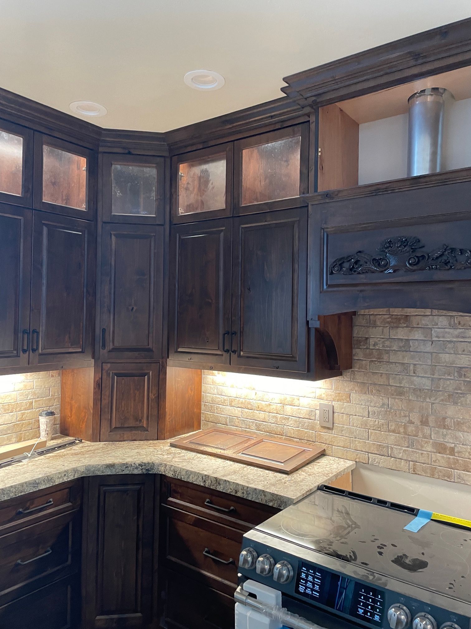 Dark wood kitchen cabinets with glass-front uppers, granite countertops, and a stainless steel range hood.