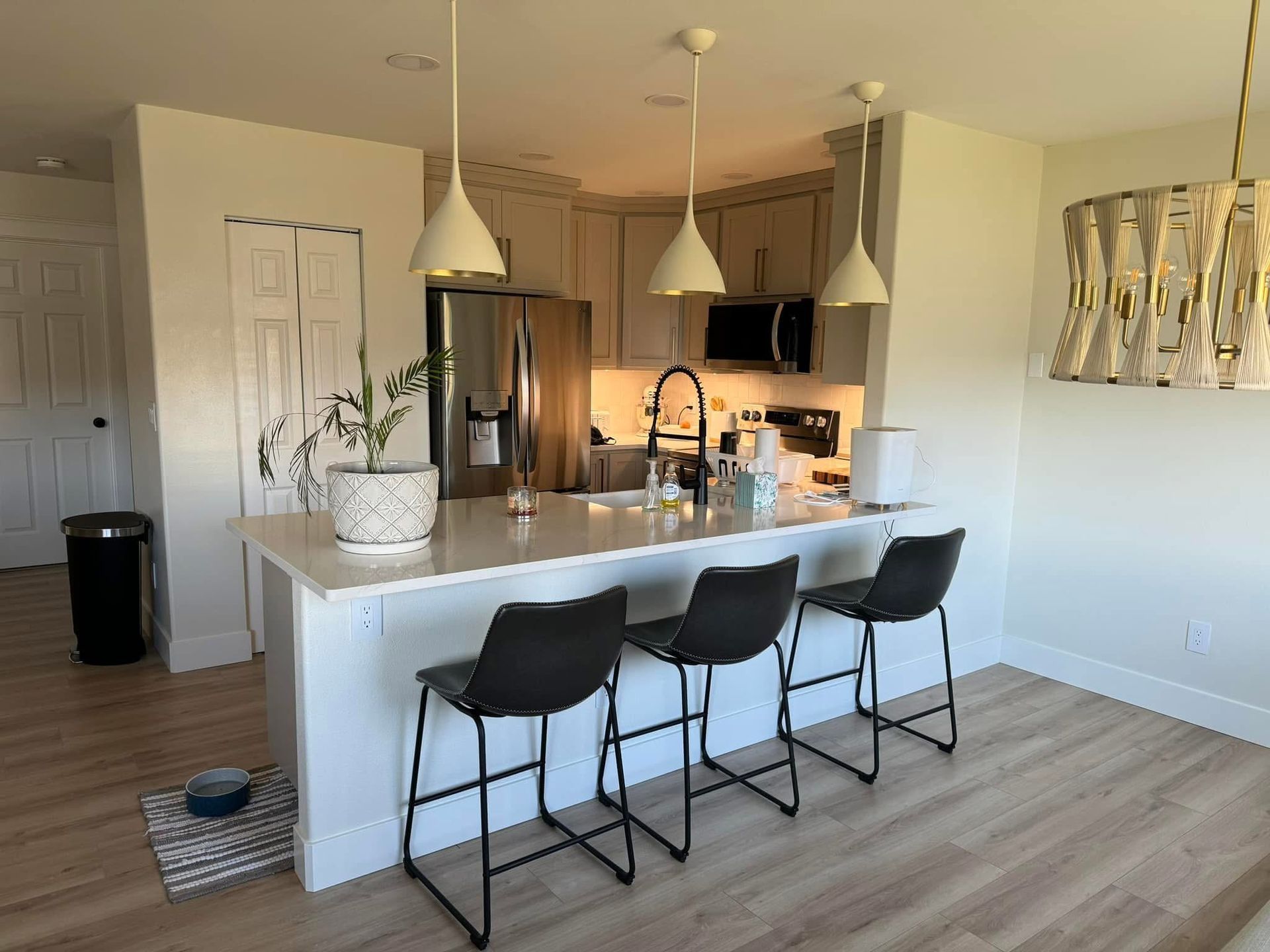 Modern kitchen with island, pendant lights, stainless steel appliances, and black bar stools.