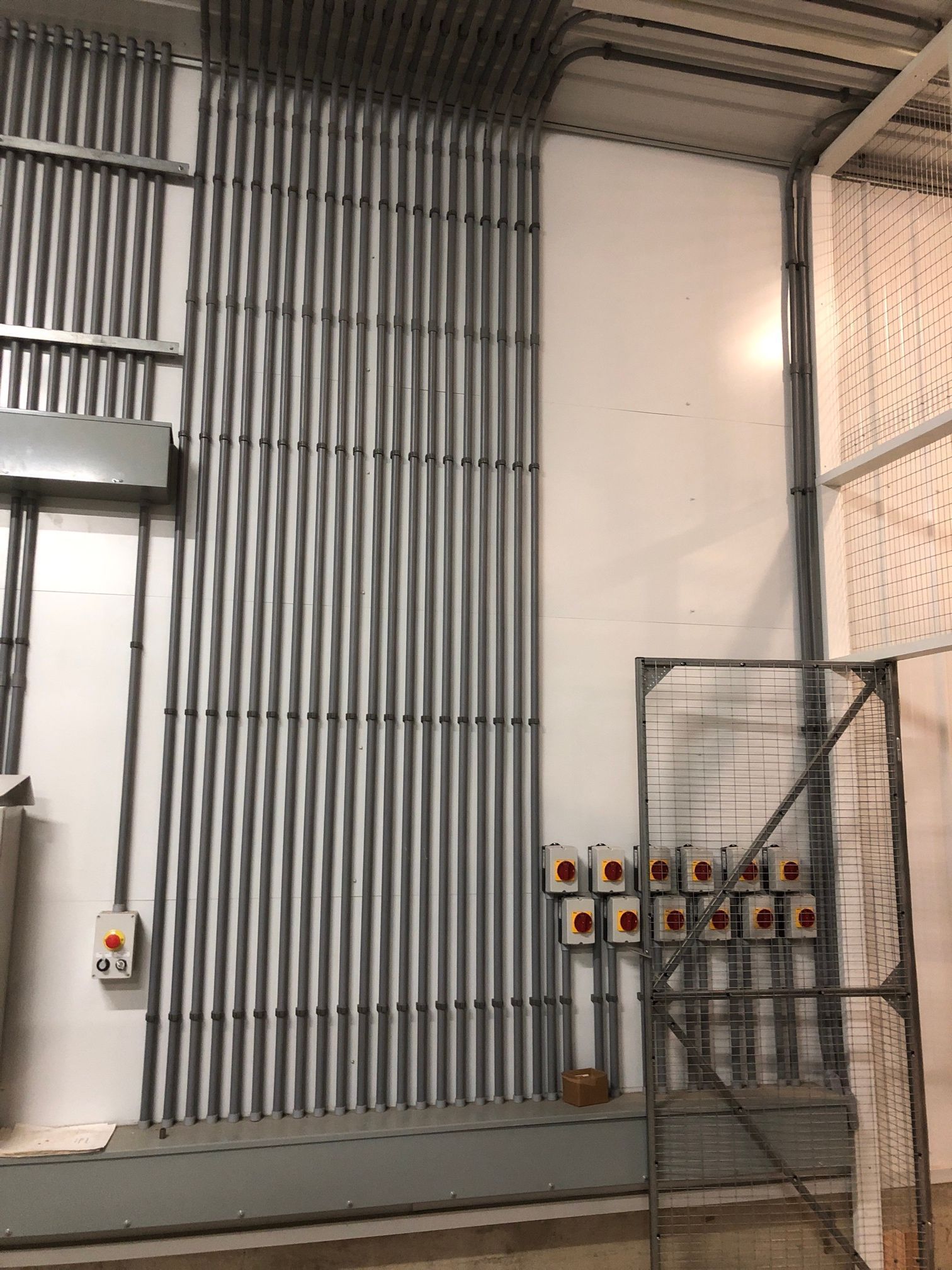 Electrical conduit runs vertically along a white wall, with control boxes and metal shelving.
