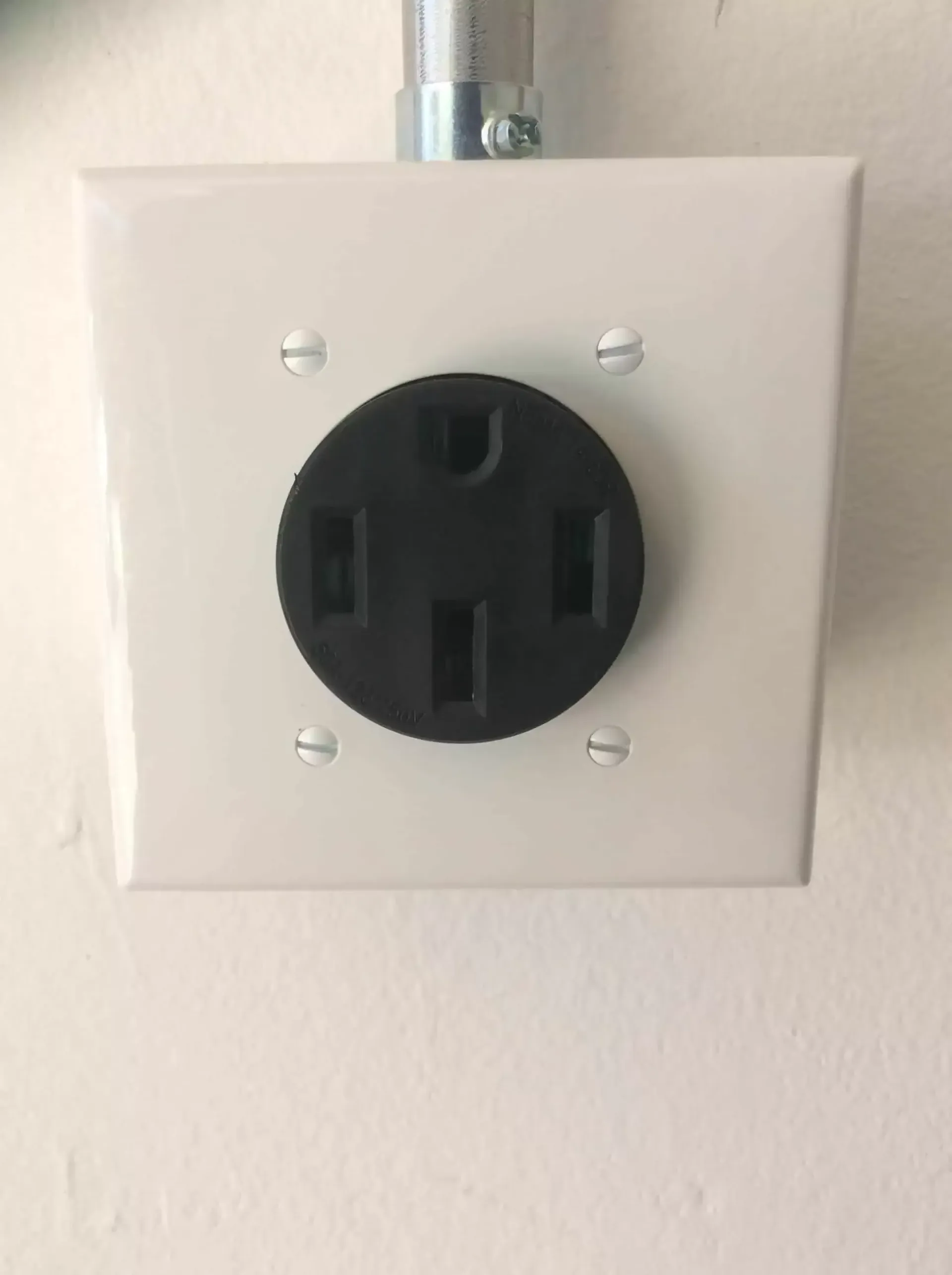 White electrical outlet cover with black, four-prong receptacle; conduit above.