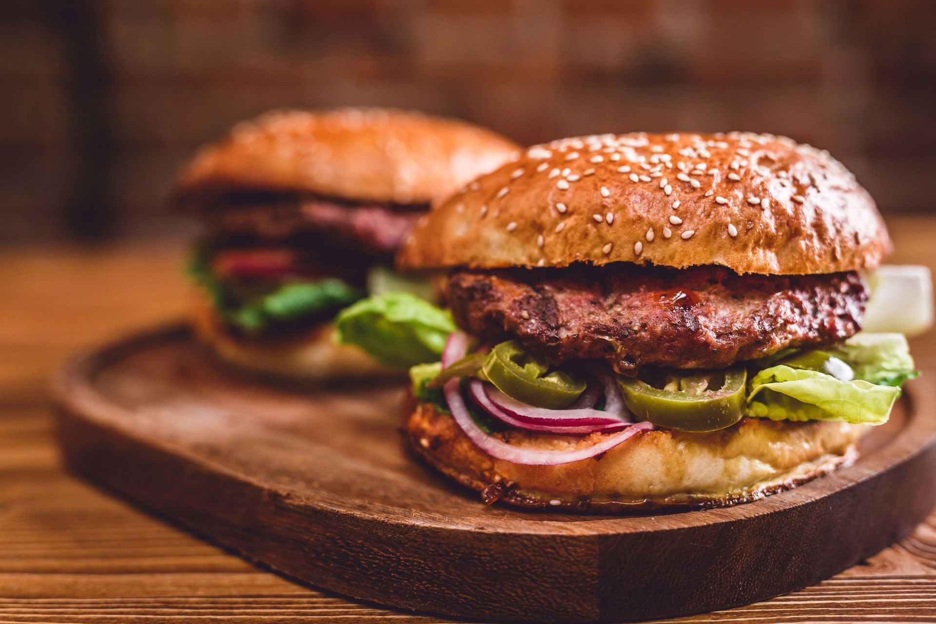 Two sesame seed burgers with toppings on a wooden board.