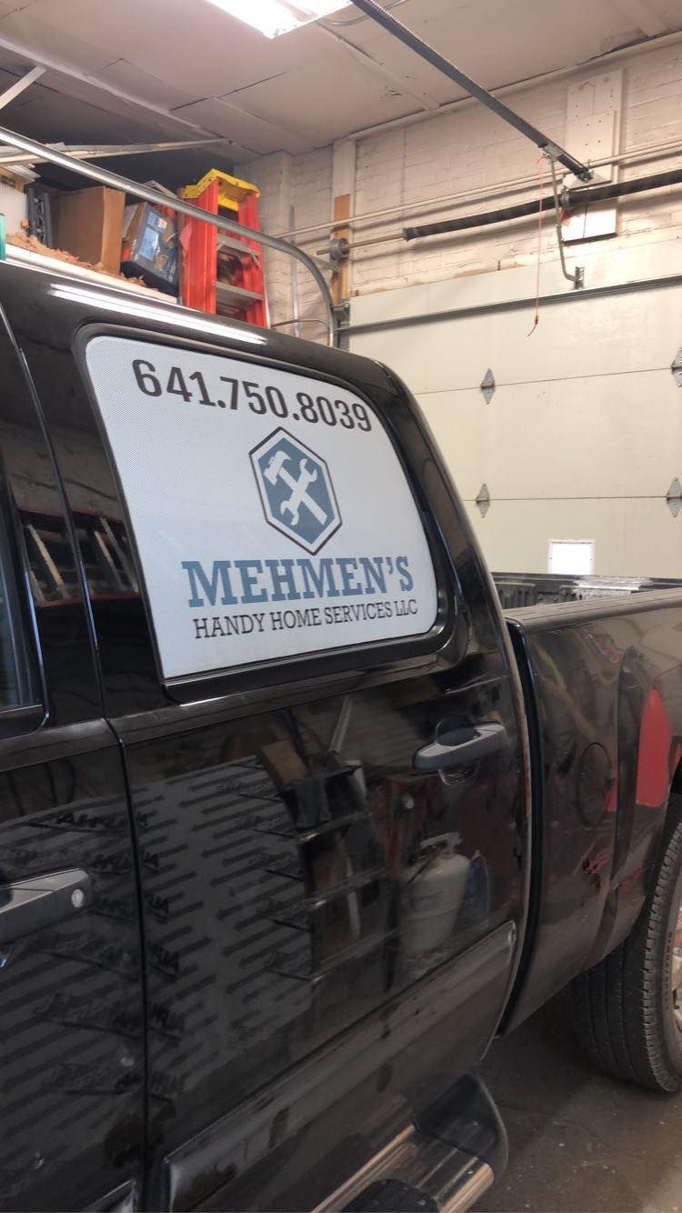 A black truck with a sign on the back window is parked in a garage.