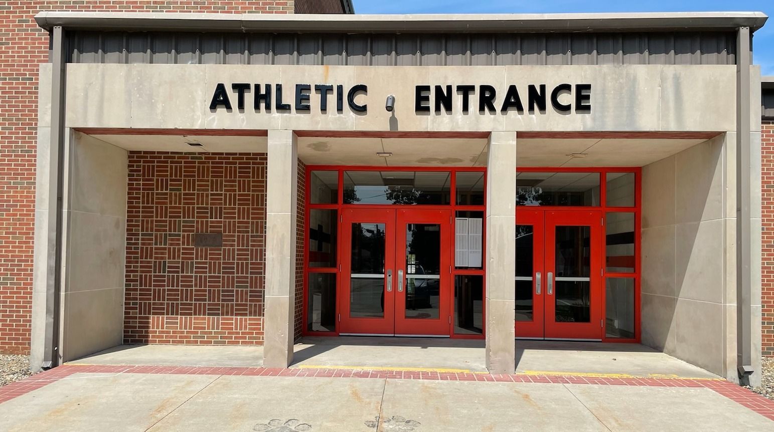 The entrance to the athletic entrance of a school with red doors.