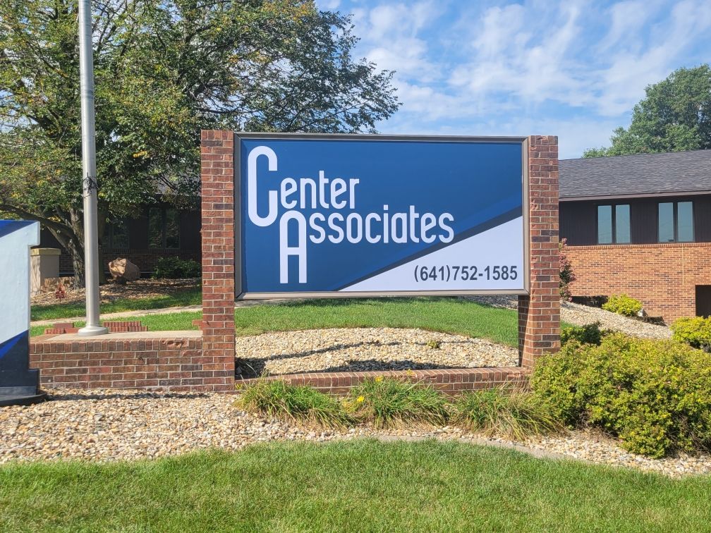 A blue and white sign for center associates is in front of a brick building.