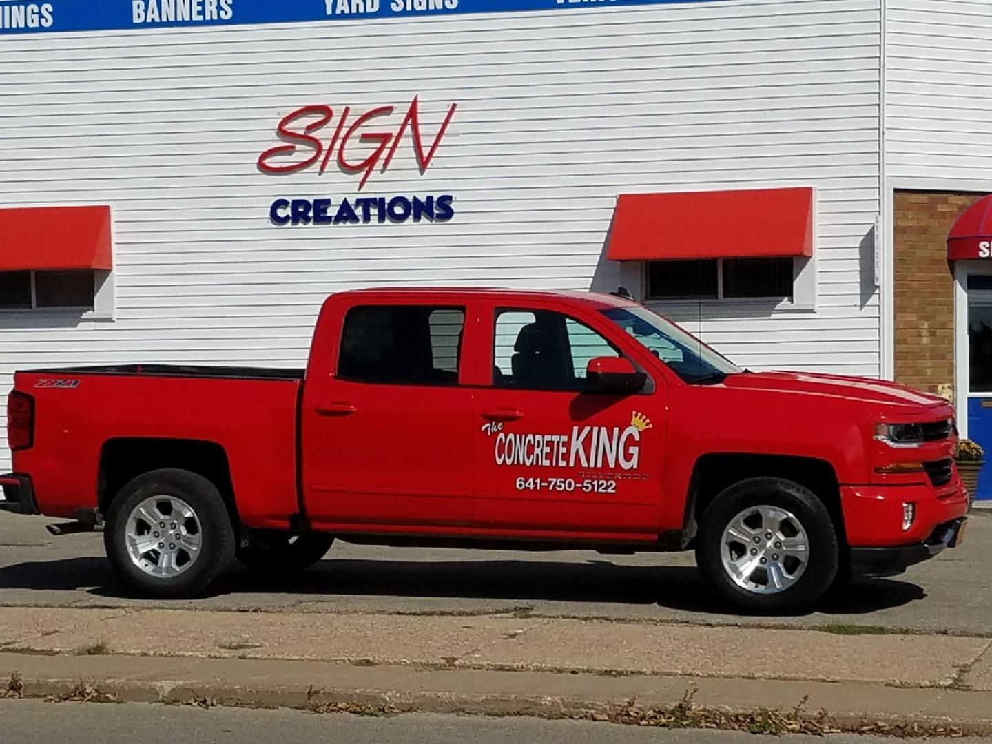 A red truck is parked in front of a sign creations building
