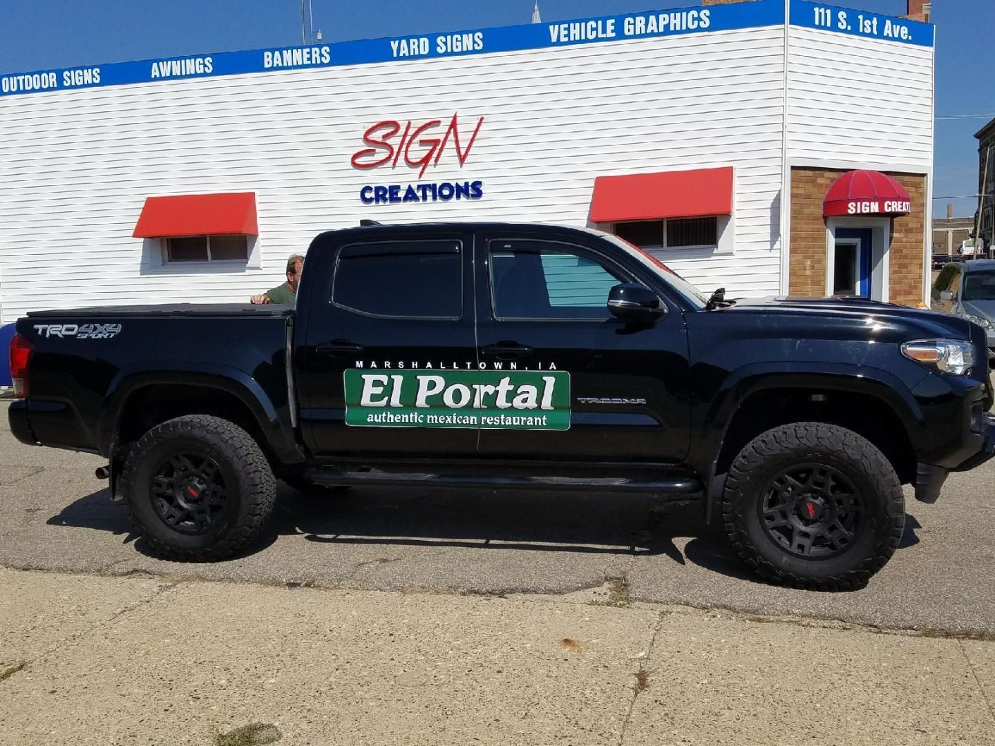 A black truck is parked in front of a sign creations building
