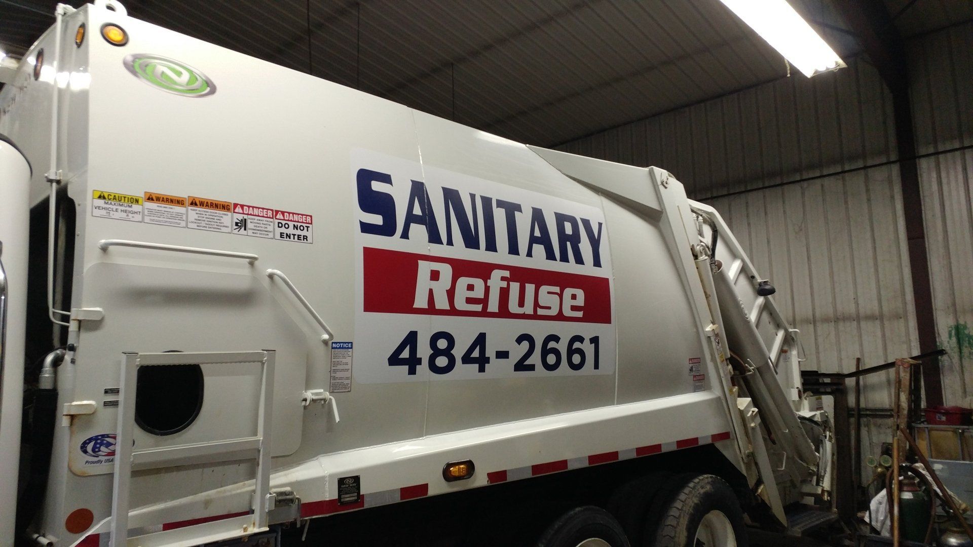 A white garbage truck that says sanitary refuse 484-2661