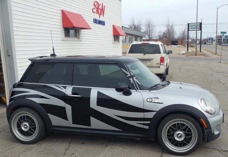 A silver and black mini cooper is parked in front of a building
