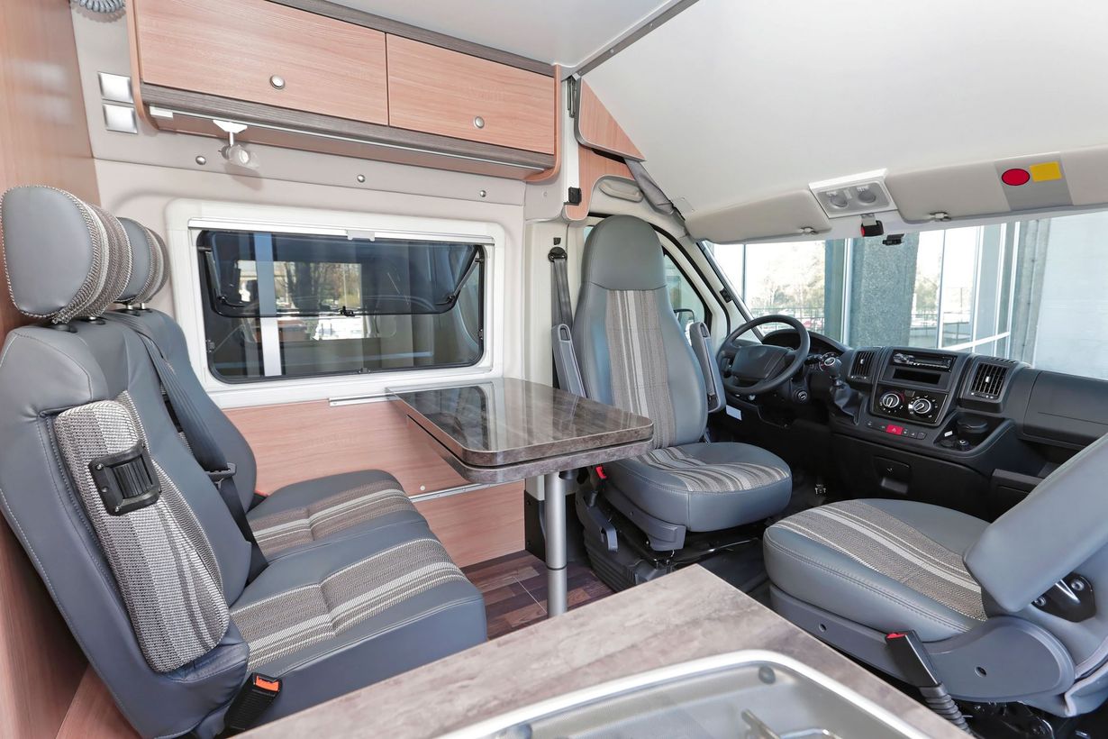 Camper van interior with front seats, dining table, and sleeping area in gray and blush tones