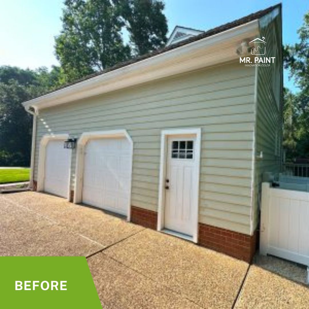 Before photo of a garage with white doors and siding, brick base, and concrete driveway.