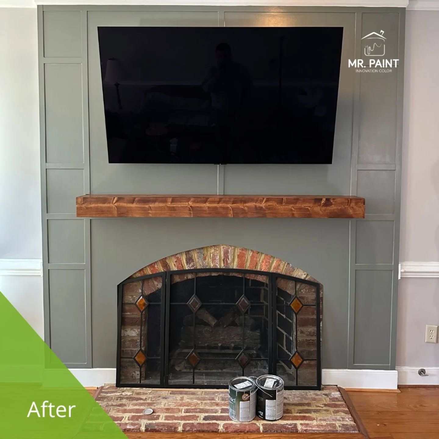 A gray painted fireplace with a mounted TV, brick hearth, and decorative paneling.
