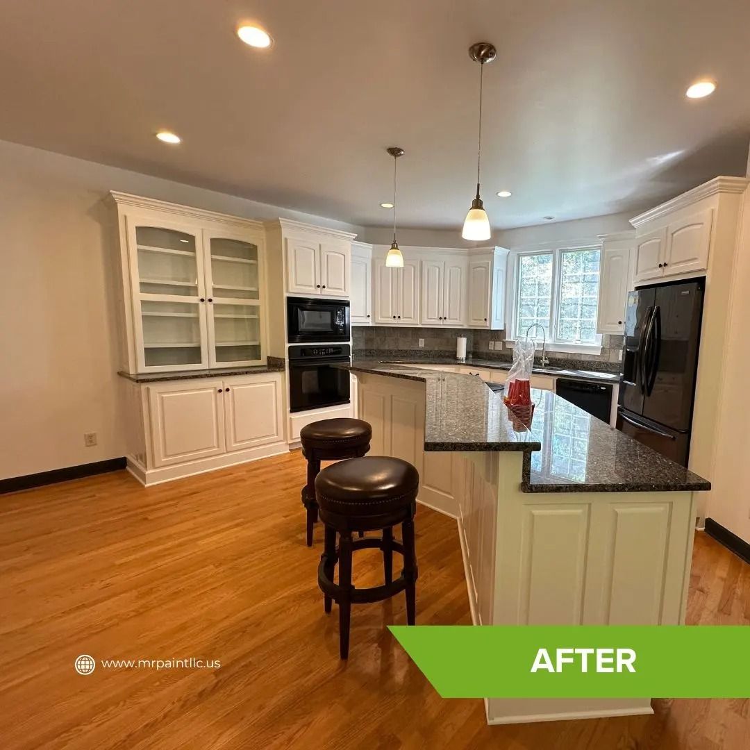 Renovated kitchen with white cabinets, dark countertops, hardwood floors, and island with stools.