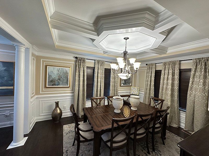 Dining room with dark wooden table and chairs, chandelier, and ornate ceiling.