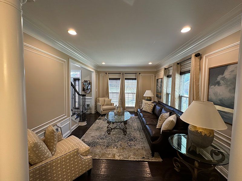 Living room with dark wood floor, brown leather sofa, patterned rug, and beige walls.