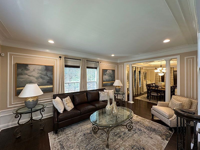 Living room with brown leather sofa, rug, paintings, and a view into a dining area.