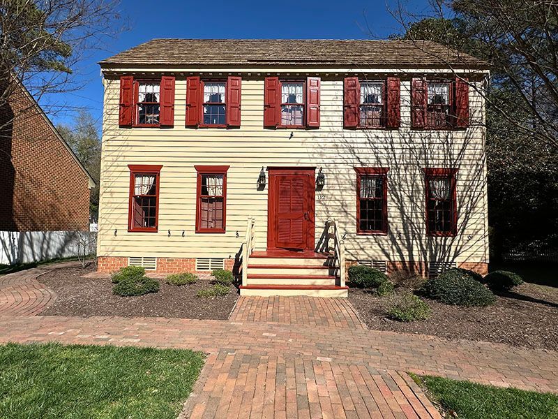 Yellow two-story house with red trim, shutters, and door, brick walkway, and green lawn.