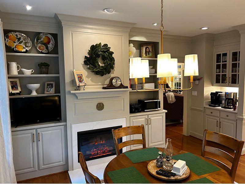 Dining room with built-in fireplace, bookshelves, round table, chandelier, and kitchen cabinets.