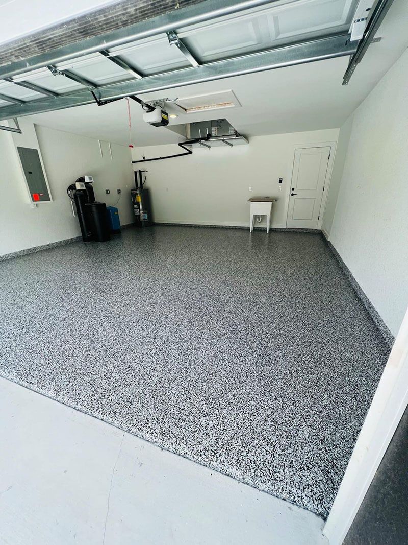 Garage interior with a speckled gray floor, white walls, and a white door. The garage door is open.