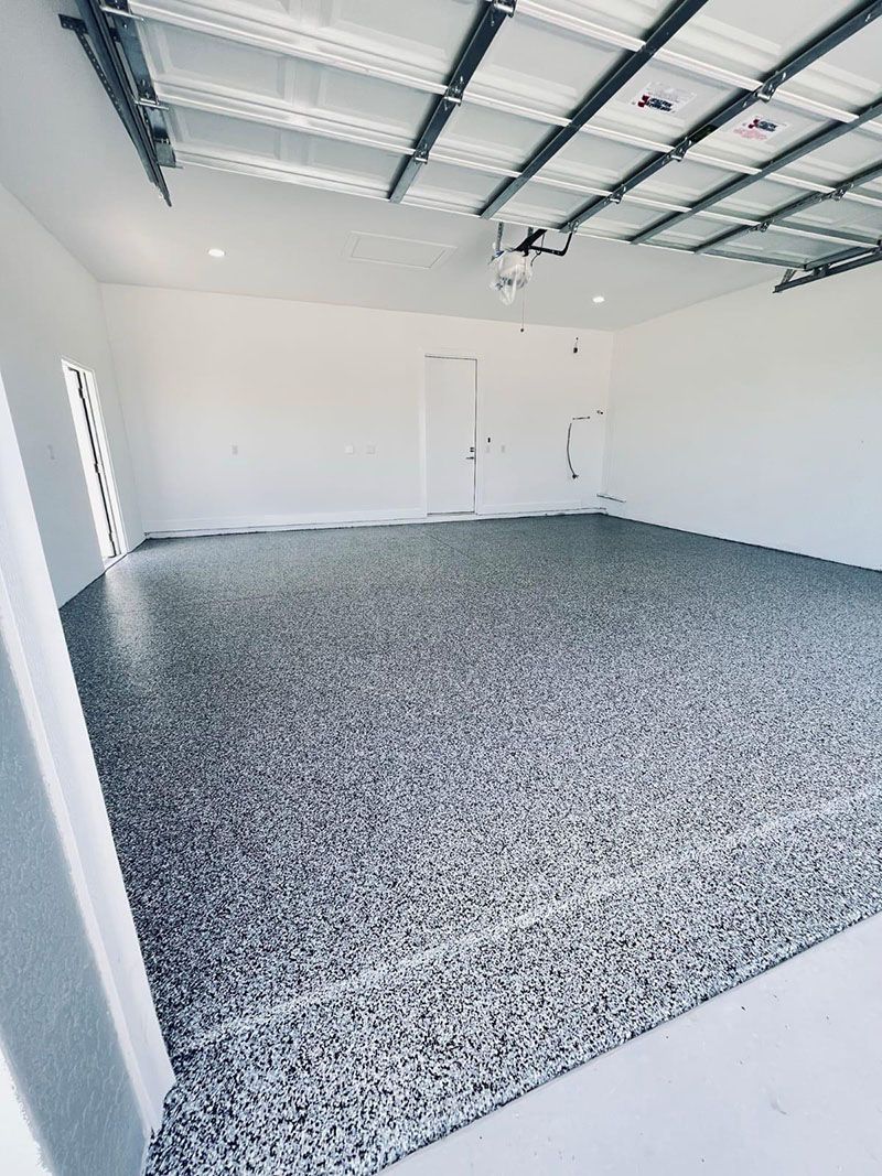 Empty garage interior with speckled gray floor and white walls. Metal ceiling beams visible.