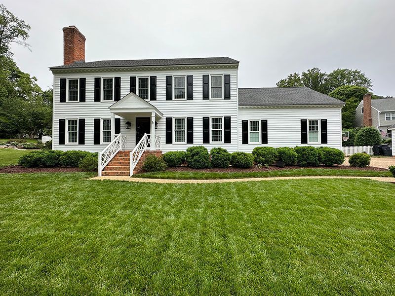 White two-story house with black shutters, brick chimney, and green lawn.