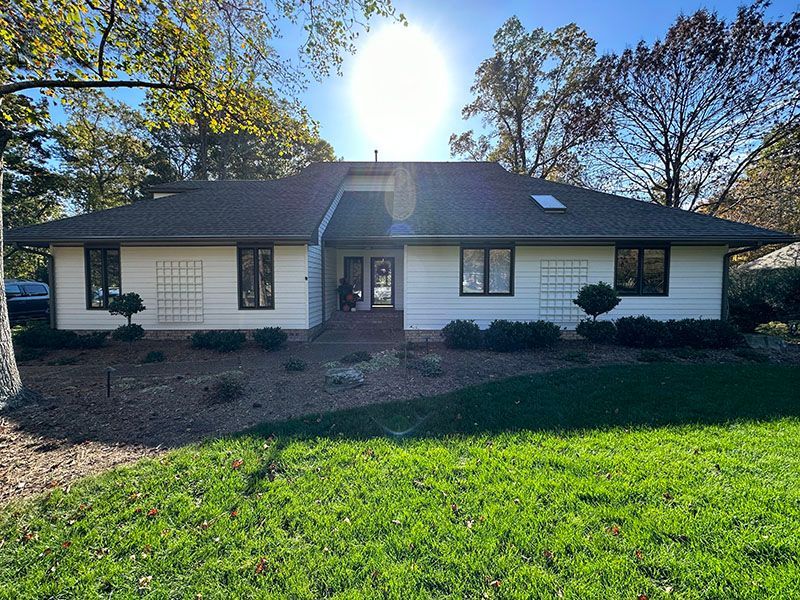 Ranch-style house with white siding, dark trim, and a lawn. Bright sun in the sky.