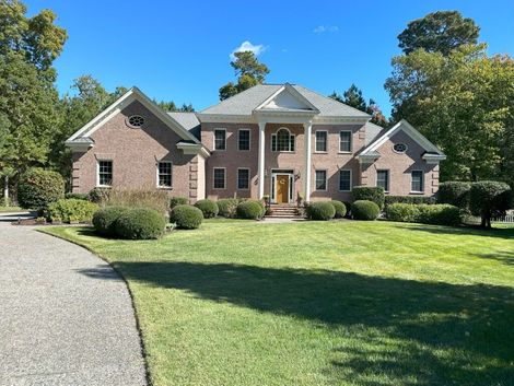 Large brick house with green lawn and gravel driveway, under a blue sky.