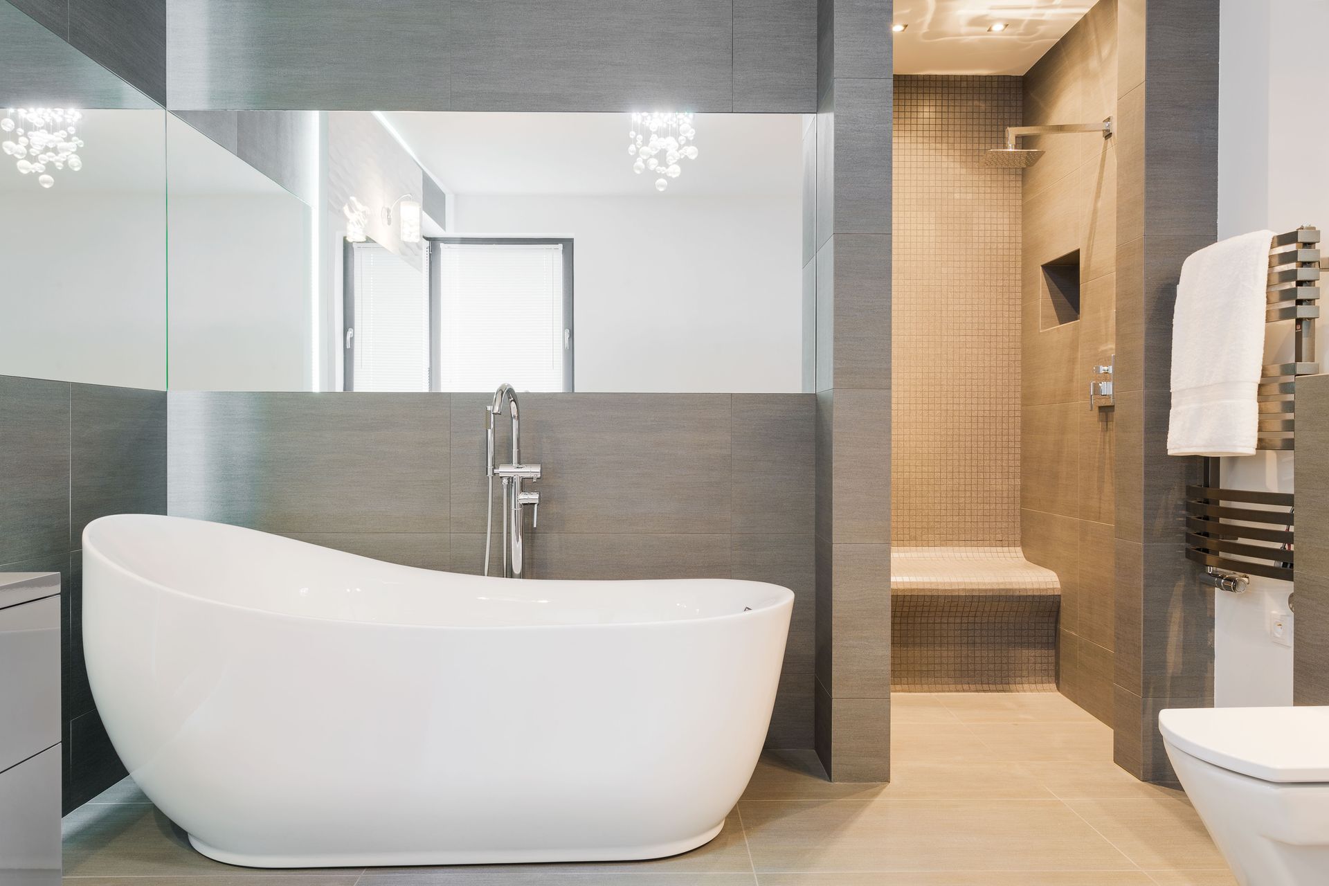 Modern bathroom with white, curved tub, shower, and gray tile walls.