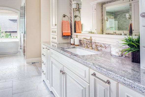 White bathroom vanity with granite countertop, sink, and mirror. Towels hanging.